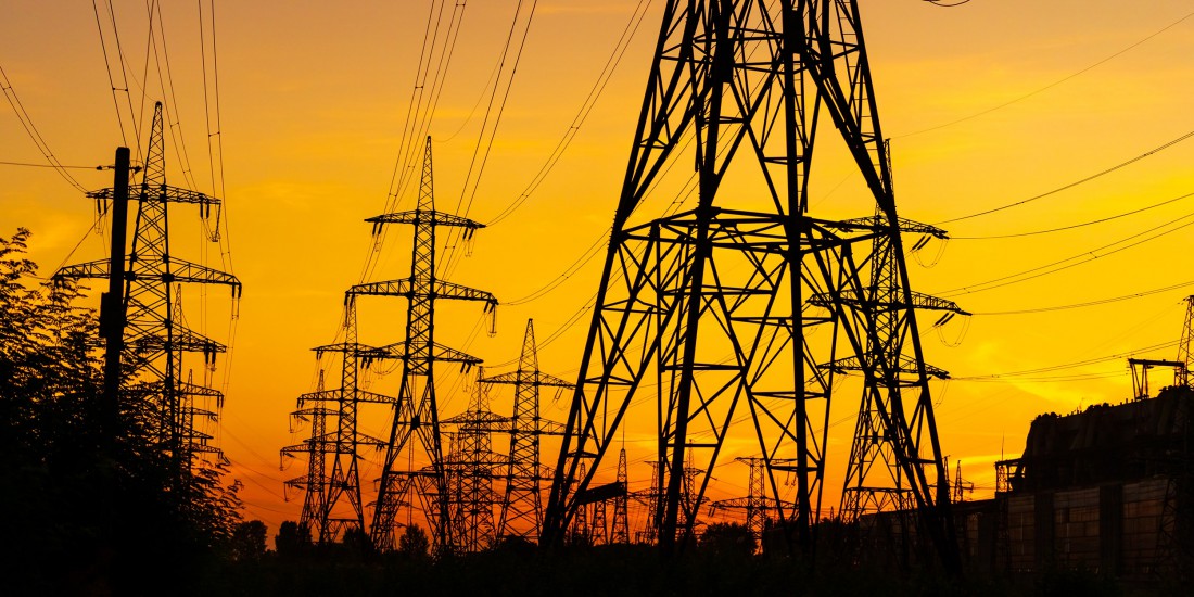 Silhouette of electricity pylons set against a vibrant yellow sunset
